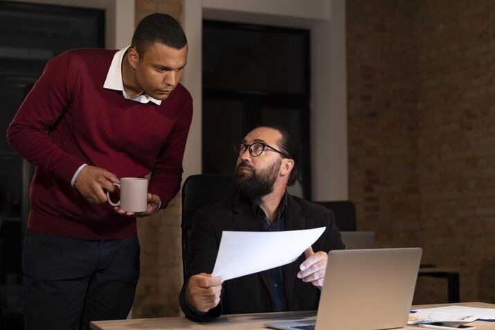 Two professionals reviewing documents and discussing workplace decisions.